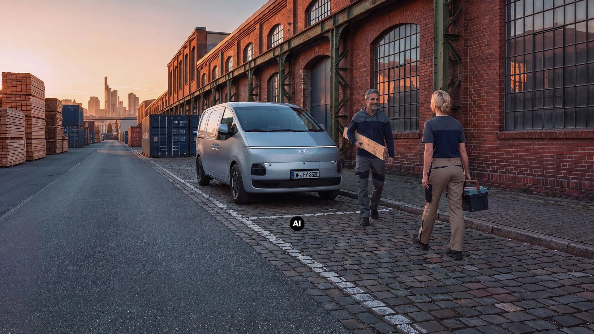 Hyundai STARIA Cargo parkerad utanför en tegelbyggnad, med två personer och arbetsutrustning bredvid bilen.