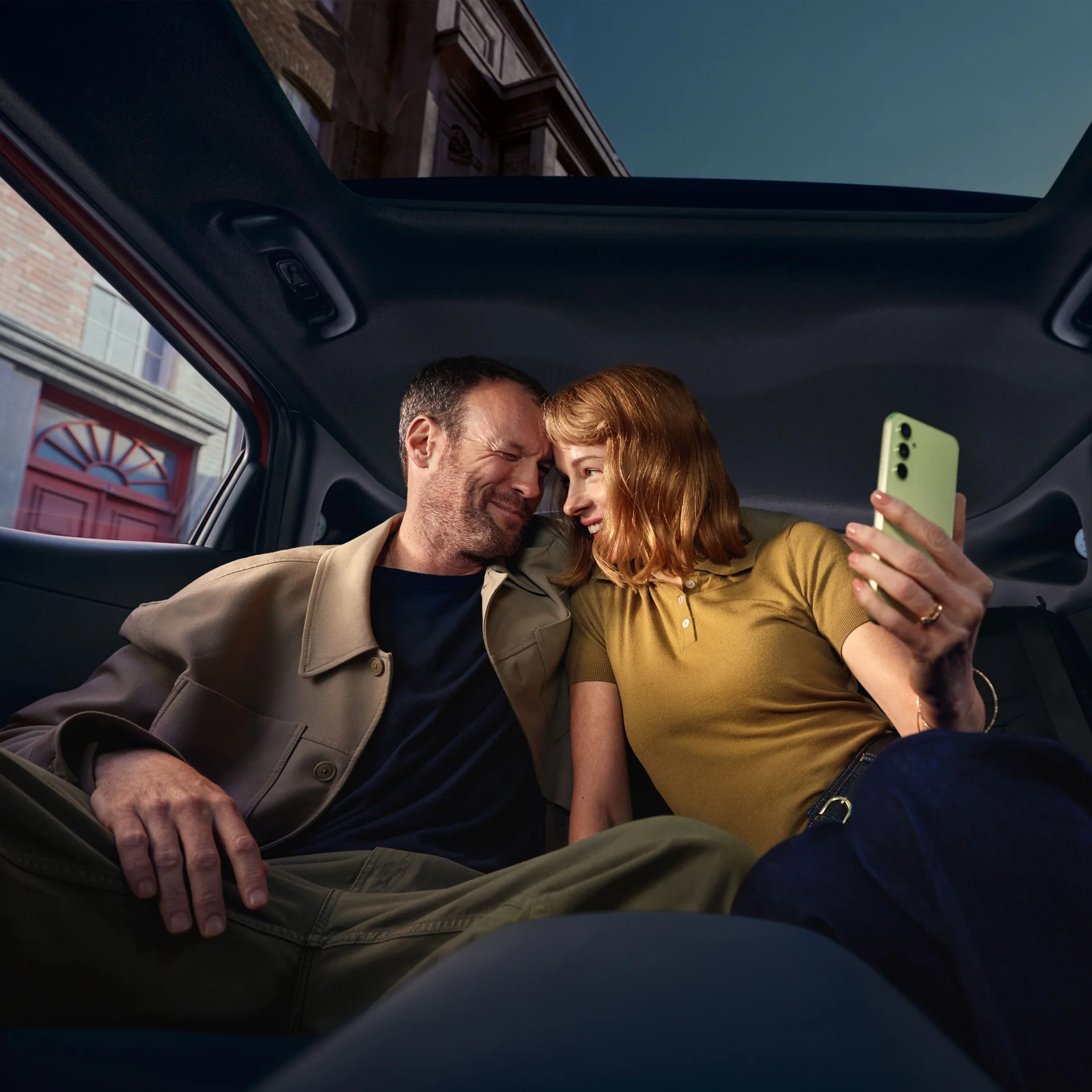 Två personer sitter i baksätet i en Hyundai och tittar på en mobiltelefon