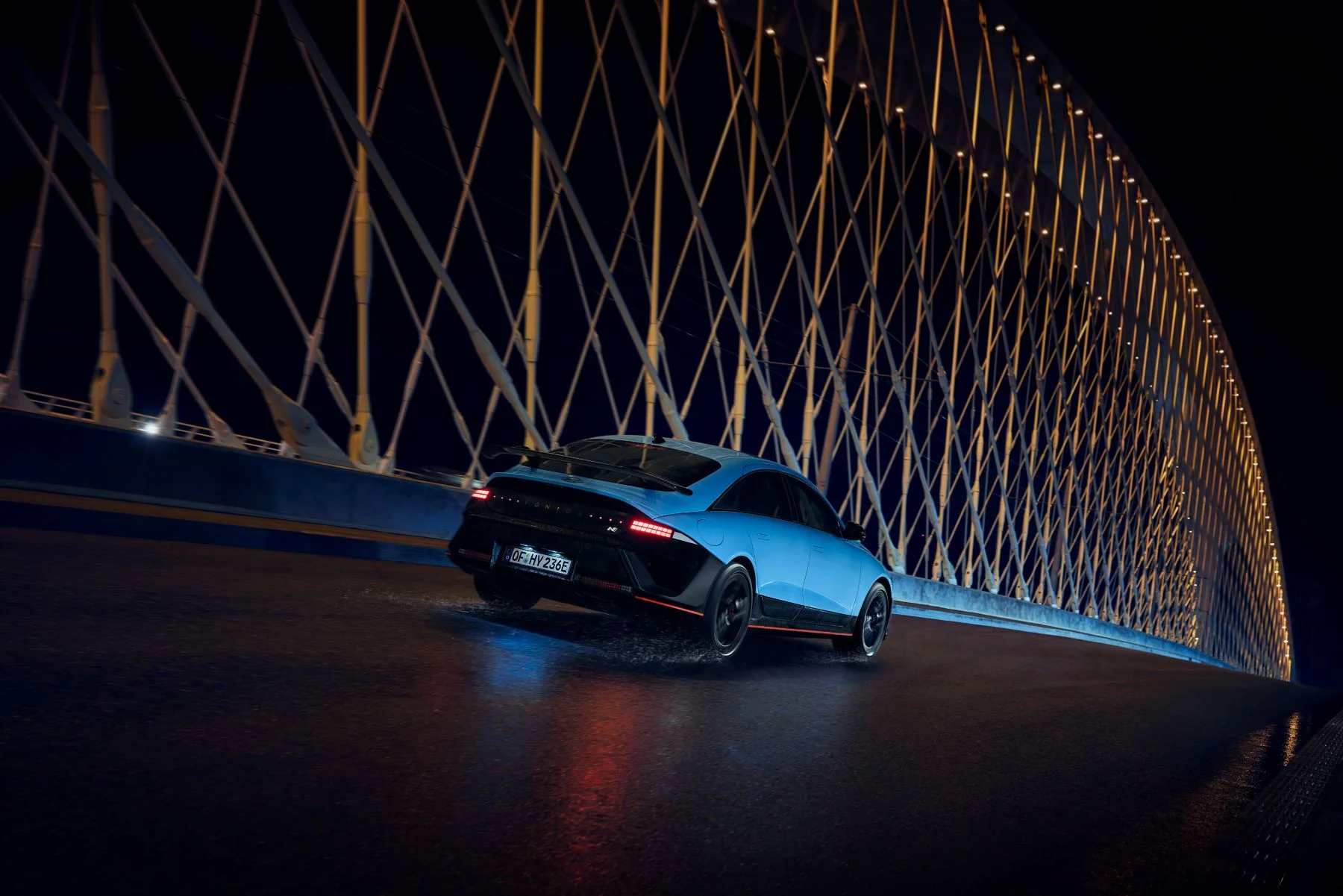 Hyundai IONIQ 6 N under körning på en upplyst bro nattetid, våt vägbana