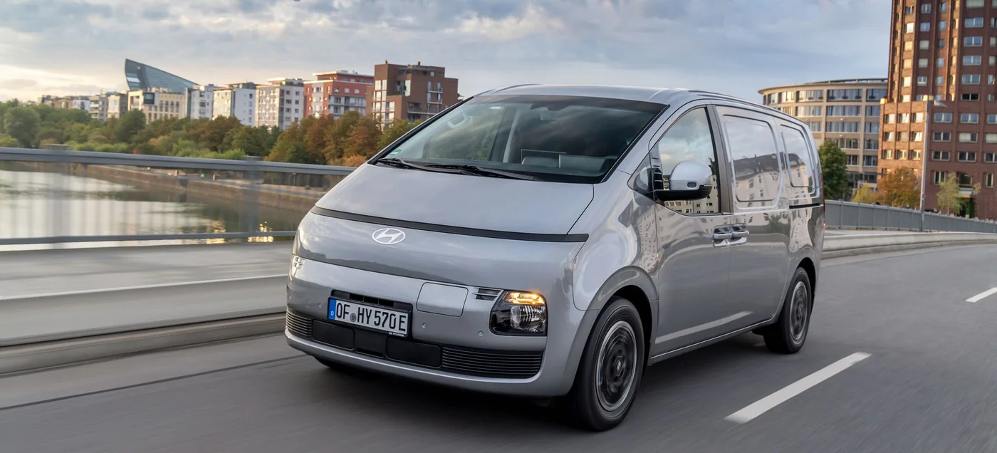 Silvergrå Hyundai STARIA Cargo kör över en bro i stadsmiljö
