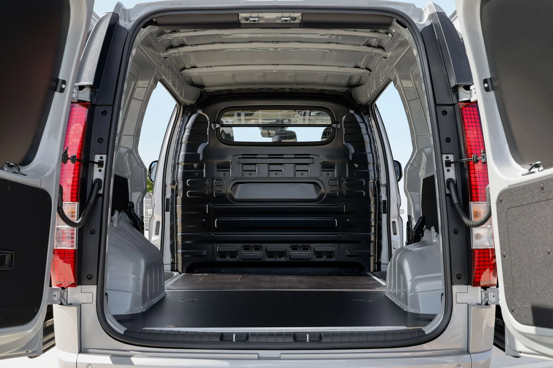 Tomt lastutrymme i Hyundai STARIA Cargo sett genom de öppna bakdörrarna, med skiljevägg i stål med fönster